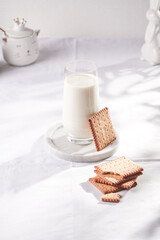 A glass of milk on a marble plate on a white table cloth, freshly baked cookies, and white easter bunnies, figurines