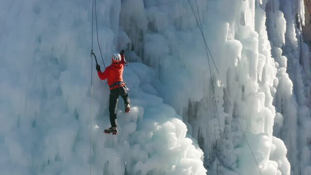 Aerial view of a frozen waterfall and rocks with climber ascending its ice-covered surface, using ice axes and crampons - Powered by Adobe