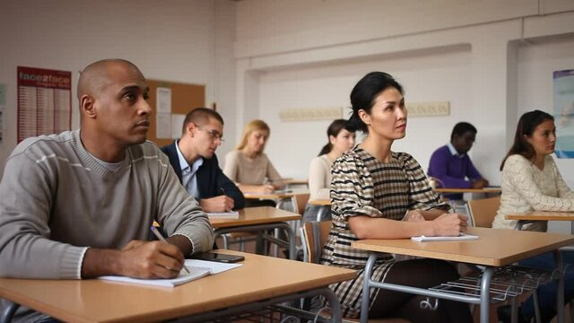  view of multiethnic group of adult people sitting in row and making notes during professional training . High quality FullHD footage