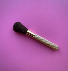 Fashionable women's makeup brush with a gold-colored handle on a pink background. A large brush for applying powder to the face. Top view, banner.