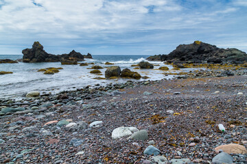 A rocky beach, with mossy rocks, along an ocean shoreline - Gros Morne, Newfoundland, Canada.