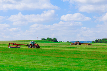 Big red tractor with two mowers mows the grass for silage