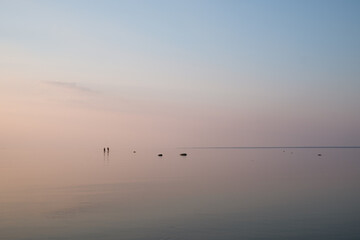 Amazing sunset with pink and blue pastel colors over the sea. Sea and sky blend together. Silhouettes of two people walking. Summer sunset at the Baltic sea, Europe. Tropical night.