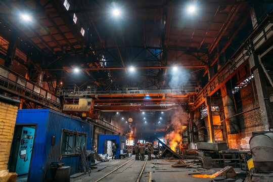 Steel production at metallurgical plant, large workshop with beam cranes and underground blast furnace.
