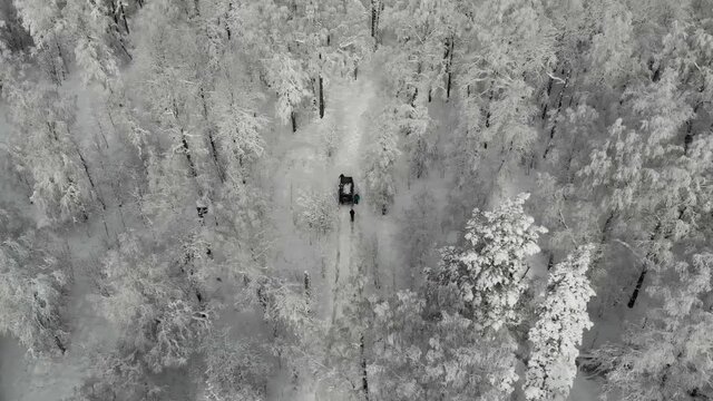 Aerial view of black SUV driving through deep white clean snow along trail in the mountains between trees. The jeep gets stuck among snowy mountains and tall pines and firs. Extreme travel, tourism