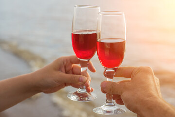 Two red wine glasses in couple hands silhouettes against sea sunset.