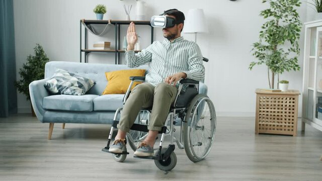 Portrait of disabled man wearing virtual reality glasses moving hands and enjoying device at home. Contemporary entertainment and physical impairment concept.
