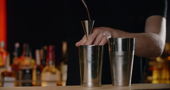 Barman pours portion of transparent alcohol from jigger to the shaker in slow motion, making the cocktail at the bar counter, 4k Prores HQ 120 fps