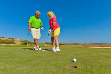 Obraz premium Active senior couple playing golf at sunset on the putting green.
