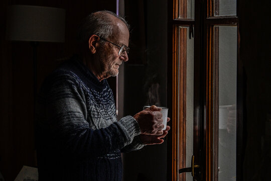 Older man with cup of tea looks melancholy out the window