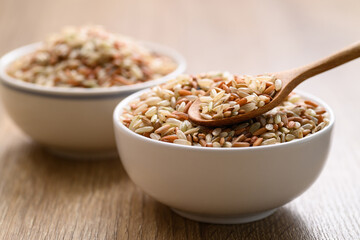 Organic Thai highland brown rice grain in a spoon and bowl on wooden table (Cargo rice, Loonzain rice or Husked rice), Healthy food