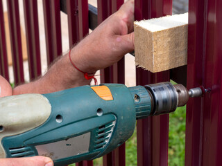 Construction of a fence in the garden. A man using a drill screws a roofing screw into a metal...
