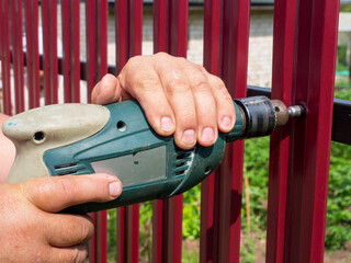 Construction of a fence in the garden. A man using a drill screws a roofing screw into a metal...