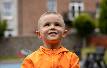 portrait of a smiling boy 6 years old in high visibility orange jacket looking up