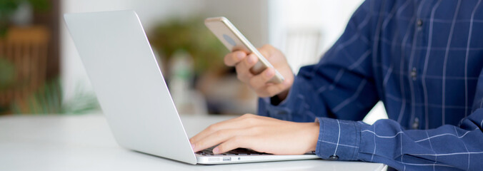 Closeup hand of young man working laptop computer and reading smartphone on internet online on desk...