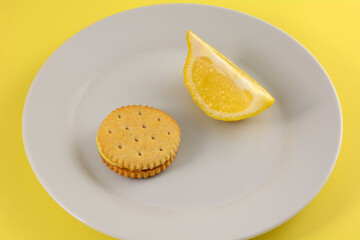 Lemon cream sandwich cookie with lemon slice on white snack plate with yellow background
