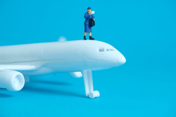 Naklejka na ściany i meble Miniature people toys conceptual photography. Airplane parcel package delivery. Postman courier with white plane, isolated on blue background.