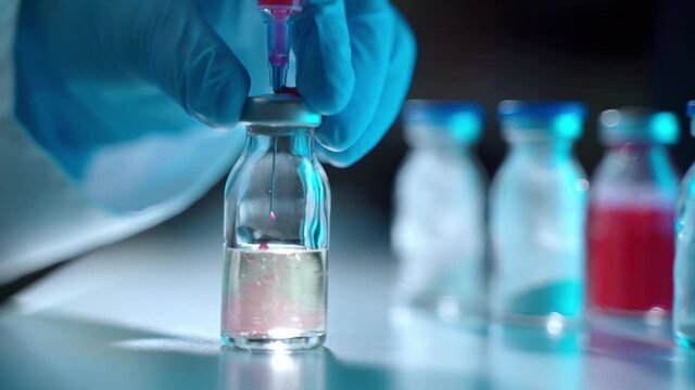 Laboratory researcher in protective gloves working with medicaments trial, chemist infusing red solution inside the vial and getting chemical compound. New medicaments developing and pharmaceutical