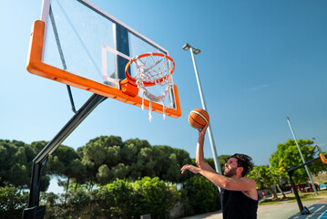 Male sportsman playing basketball throwing the ball at playground, doing successfully slam dunk...