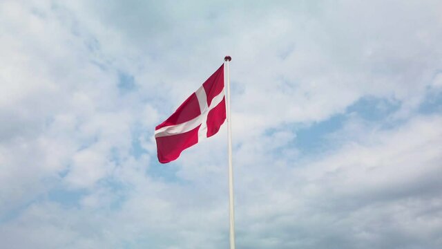 Danish flag waving in the wind, on a blue sky with white clouds, on a beautiful summer day. Just the top of the flag pole and the whole flag is in frame. 4K