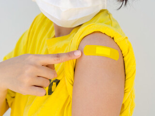 Vaccinations, bandage plaster on vaccinated women's arm concept. Hand pointing on yellow adhesive...