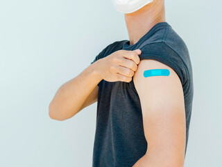 Vaccinations, bandage on vaccinated people concept. Blue bandage on man shoulder who wearing grey...