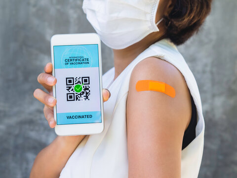 International certificate of vaccination, smart digital passport with QR code on smartphone screen showing by the vaccinated woman who wearing face mask and orange bandage plaster on his shoulder.
