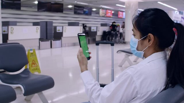 4K Asian tourist women wear protective face masks for outbreak coronavirus sit on social distancing chair use smartphone for contact with friend or family. Women use mobile phone with green screens.
