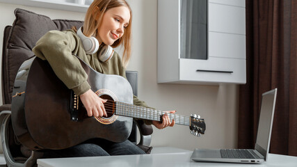 Teenager girl learning play guitar at home using online lessons. Hobby remote musical education acoustic guitar. Young woman play acoustic guitar at home for online audience on laptop. Long web banner
