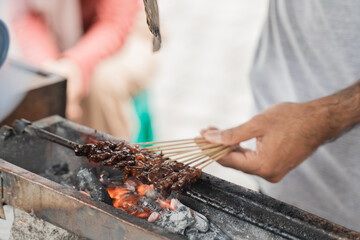 close up of hand with traditional chicken satay skewer in charcoal grill
