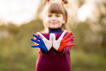 Freedom France concept. Cute child forming flying bird gesture with painted in France colors hands at bright sunset background. July 14, National Day of France