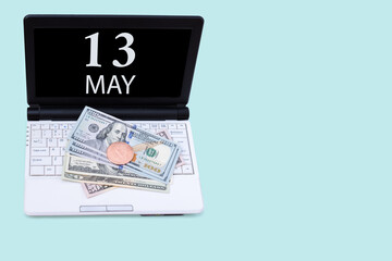 Fototapeta na wymiar Laptop with the date of 13 may and cryptocurrency Bitcoin, dollars on a blue background. Buy or sell cryptocurrency. Stock market concept.
