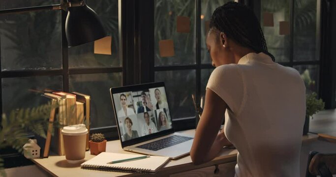 Young African American woman talking with colleagues online via video calling on laptop computer at home during pandemic, dolly shot  