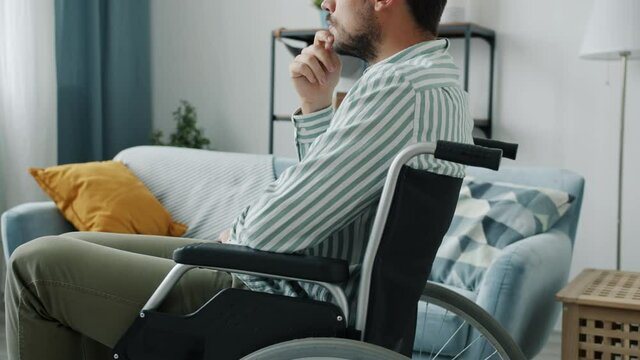Side view of pensive disabled person in wheelchair thinking indoors in apartment alone. Unhappy handicapped people and leisure time concept.
