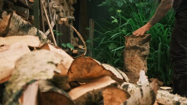 A man cannot split a log with a hammer and wedge in any way. A man in a summer garden next to a woodshed splits a log with a wood splitter and a sledgehammer. Close-up
