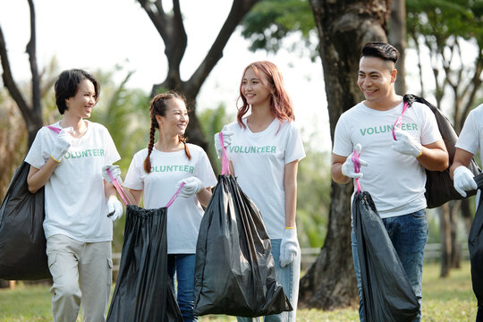 Group of cheerful friends volunteering in local park and picking up trash to clean the ground