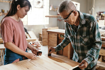 Senior experienced carpenter showing aprentice how to cover wooden board with lacquer to protect it and give shine