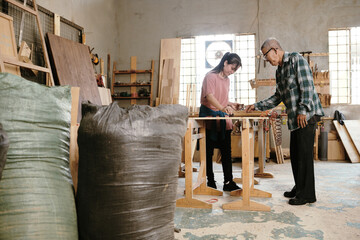 Experienced senior carpenter controlling his daughter applying oil on sanded wooden board