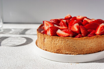 Summer strawberry pie on white table with hard shadows of glass goblet, close-up