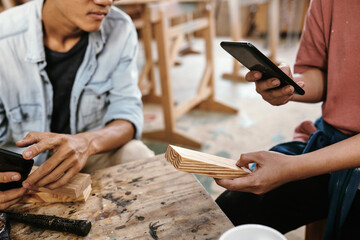 Hands of young female carpener taking photo of wooden sample and uploading on social media to get more orders