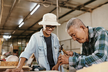 Smiling senior carpenter showing grandson how to work with chilsel and hammer when carving wood