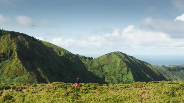 Drone shot of male traveller walking on path of Miradouro do Cerrado das Freiras, Sao Miguel island, Azores, Portugal, Europe. Young man enjoying hike in summer mountains, 4k footage