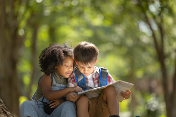  Multi-ethnic children in casual clothing sitting on tree roots, looking at the map with...