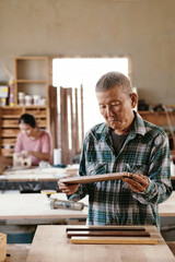 Pensive concentrated carpenter checking quality of walnut and maple wooden pieces fused together