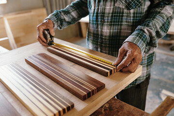 Hands of elderly carpenter measuring walnut and maple wooden pieces fused together for making edge...