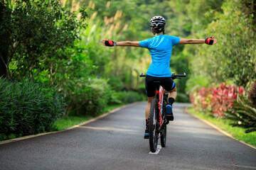 Woman no handed cycling on tropical park trail in summer