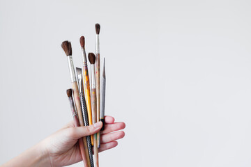 The hand of a girl artist holds a brush for painting on a white background.