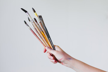 The hand of a girl artist holds a brush for painting on a white background.