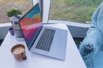 And the tent on the table is a laptop, a coffee pot, a cup of coffee. Good morning concept. Summer vacation in nature.