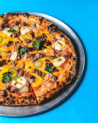 Whole cheese and meat pizza over blue background. Pizza with onions and pickles served on a metal tray.